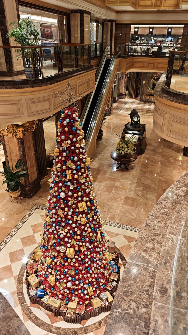 A tall Christmas tree with red and gold baubles in the marble lobby of Crowne Plaza Shanghai Nanjing Road, seen from above