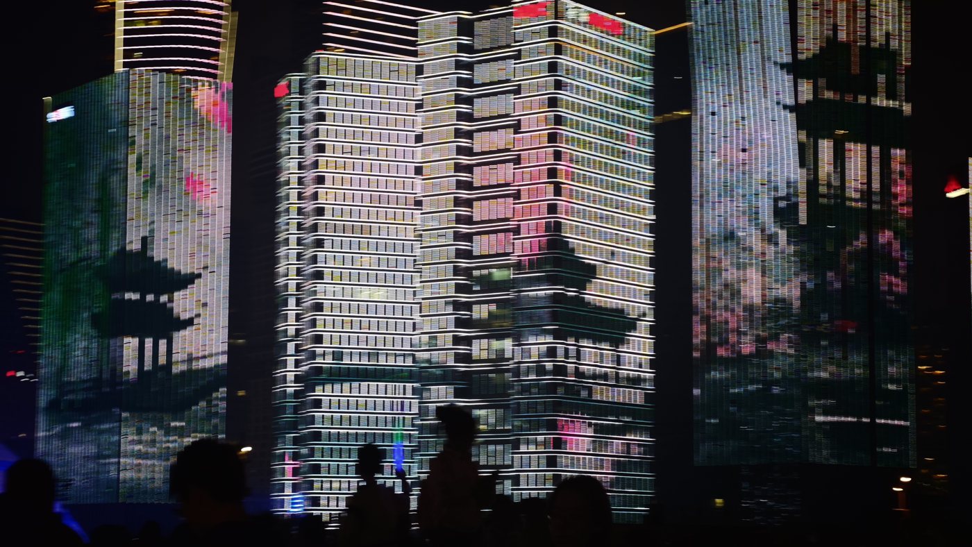 Hangzhou towers covered by a light show of pagoda roofs and pink and green patterns on their glass sides