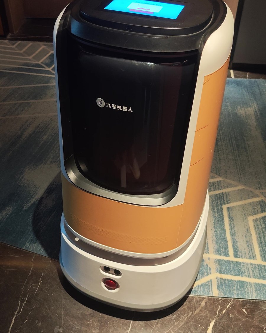 An orange and white food delivery robot waiting in a hotel corridor in Shanghai