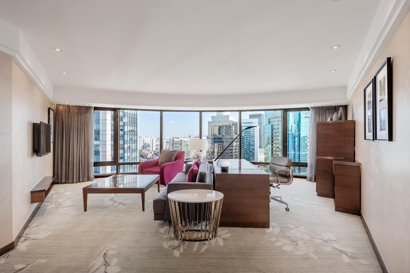 Living room of the Diplomatic Suite at InterContinental Shanghai Pudong with a desk, a pink chair and curved windows over the city