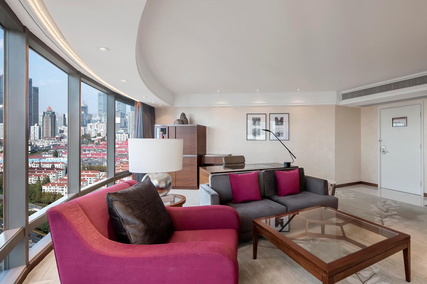 Sitting area of the Diplomatic Suite at InterContinental Shanghai Pudong with a pink sofa, a grey sofa and rooftops through the window
