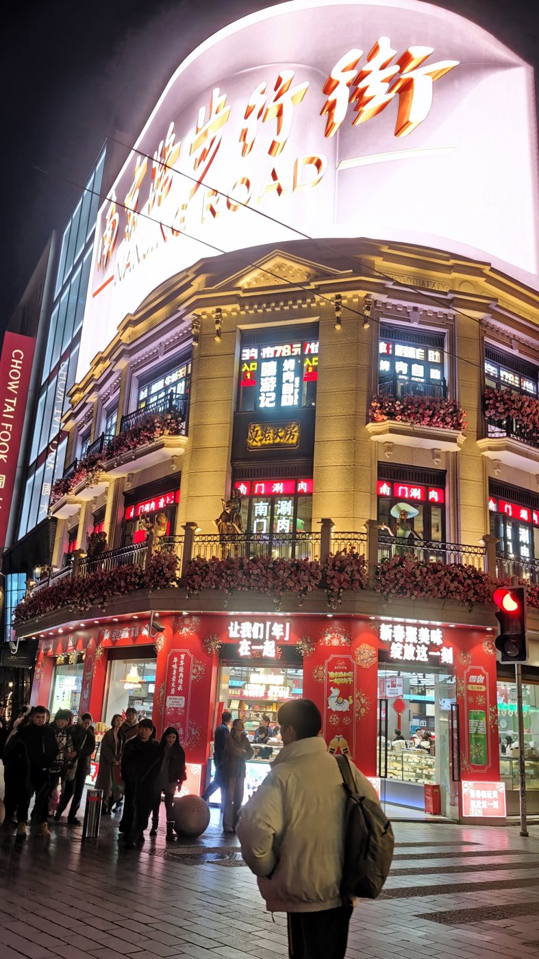 A curved corner building on Nanjing Road lit gold and red under a large glowing sign at night