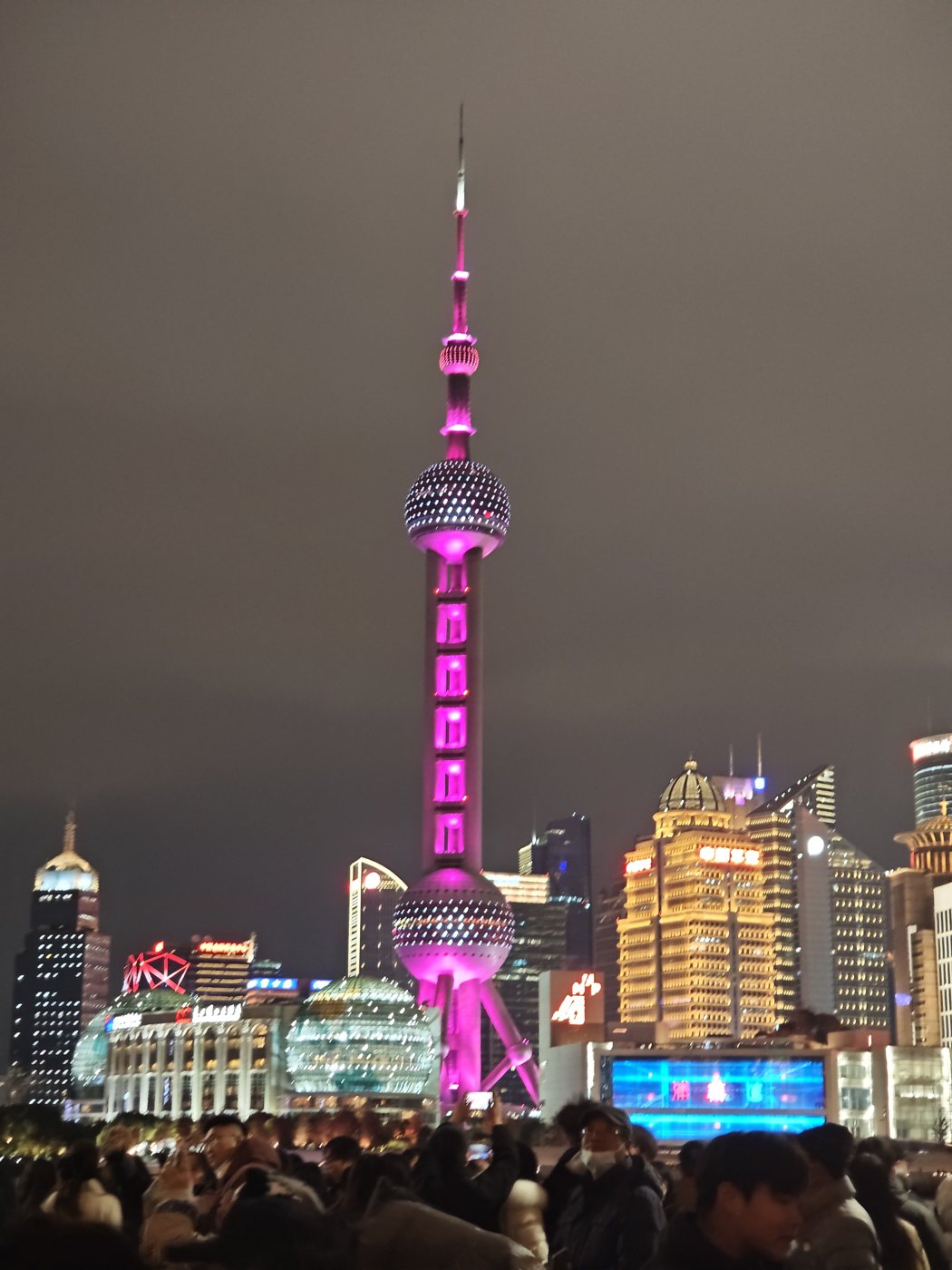 The Oriental Pearl Tower lit pink above the crowd on the Bund at night