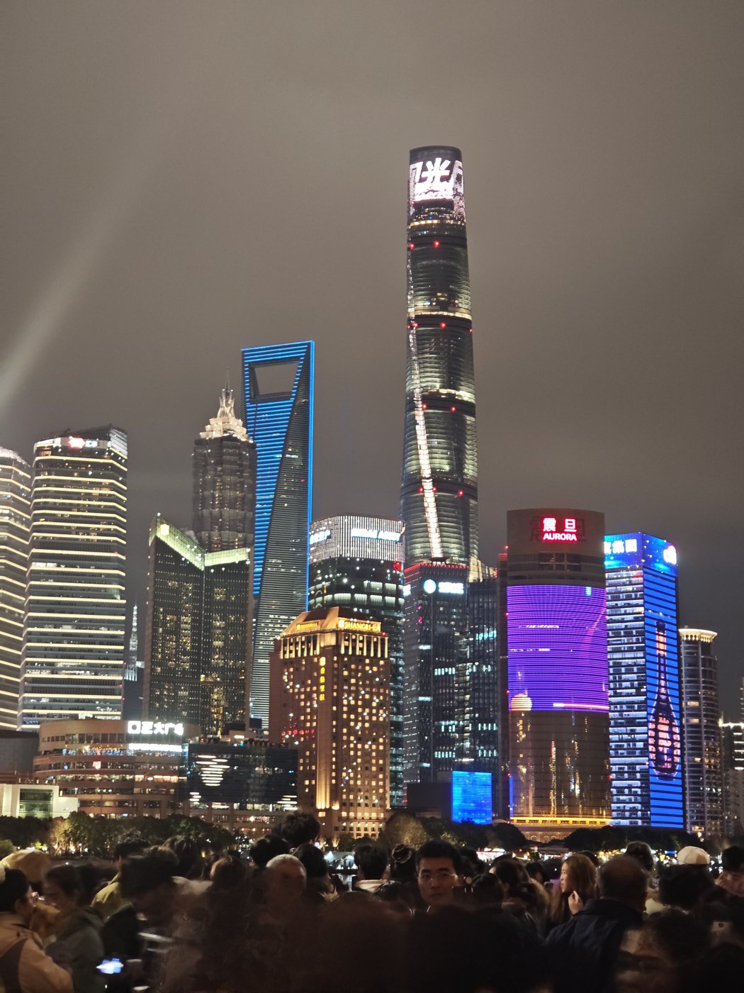 Shanghai Tower and the Pudong skyline lit in blue and purple, seen from the Bund at night