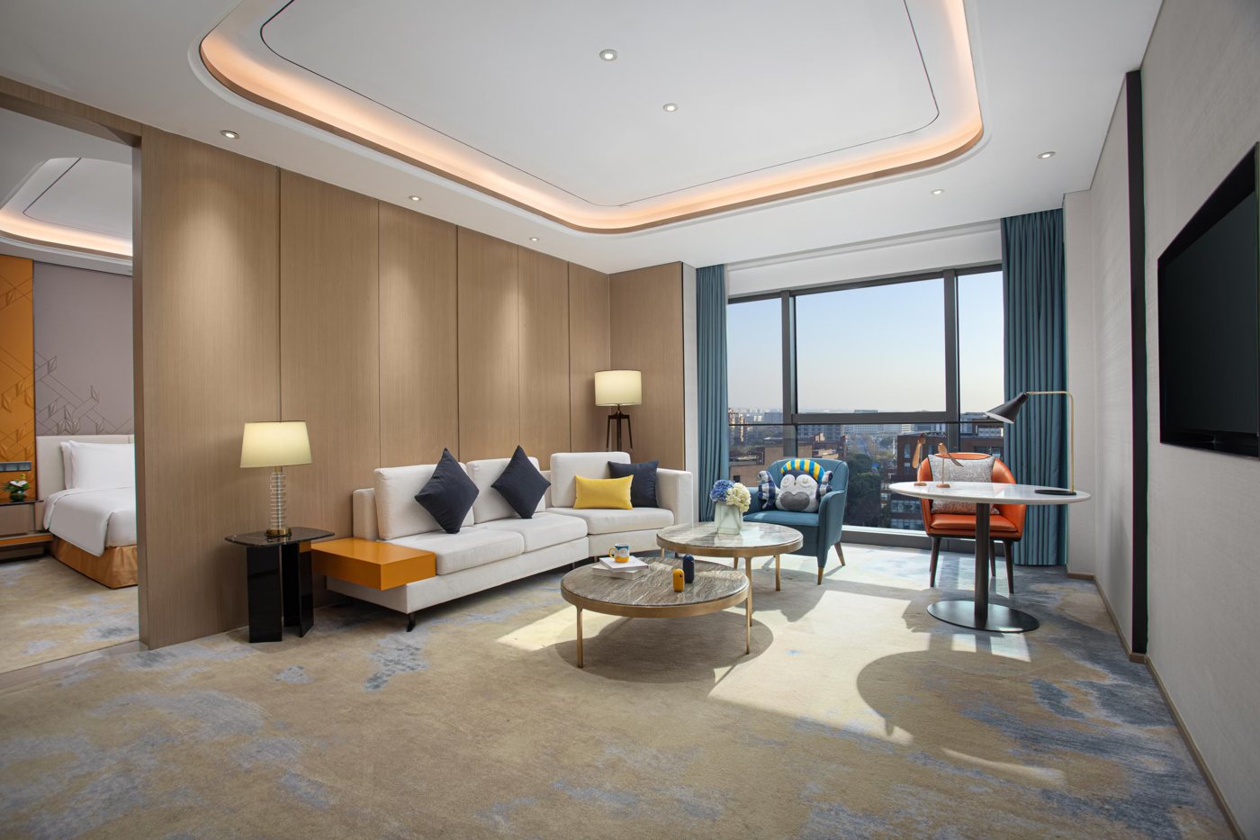 Living area of the room at voco Shanghai Hongqiao Hub with a white sofa, round tables, a big window and the bed through an opening